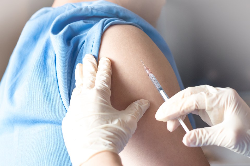 A doctor or nurse in white medical gloves injecting a vaccine into a patient's arm.