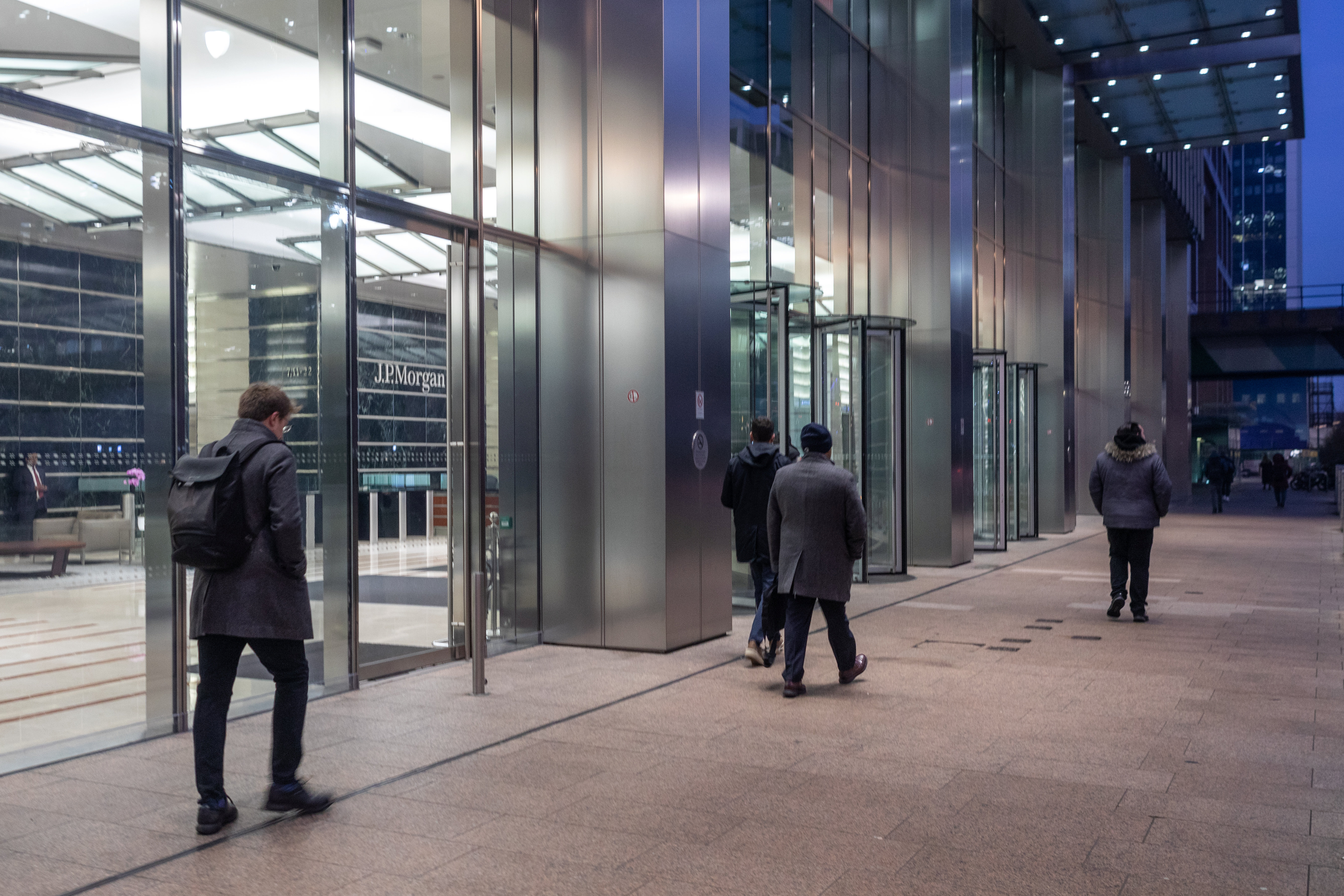 People walk past the J.P. Morgan building with large windows and revolving doors.