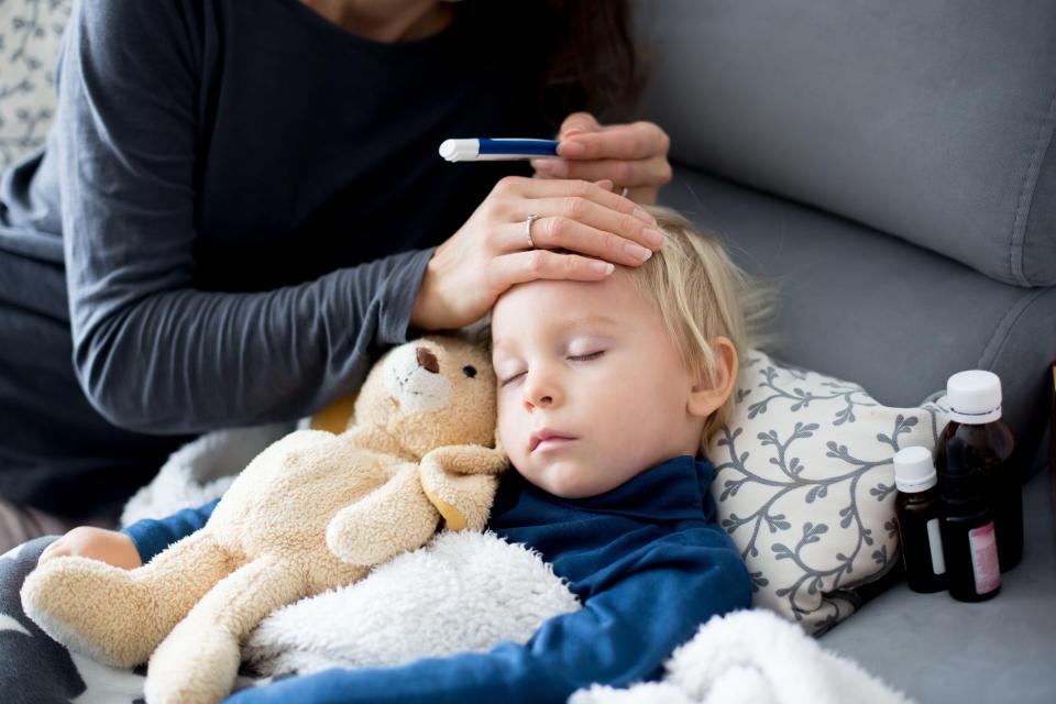 Blond toddler boy, sleeping on the couch in living room, lying down with fever, mom checking on him