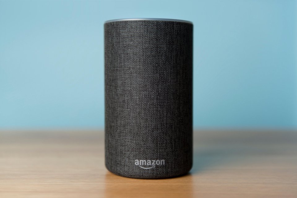 Charcoal Amazon Echo (2nd generation) smart speaker on a wooden table with a blue wall in the background.