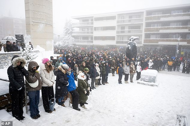 People observe a minute of silence as they watch the official commemorative ceremony on a giant screen in front of the St. Christopher Chapel in Crans-Montana