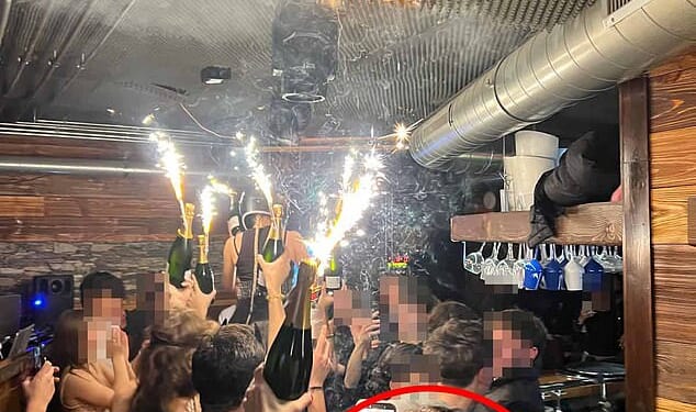 In a clip taken from the deadly night at Le Constellation in Crans-Montana, a woman, believed to be bar owner Jessica Moretti, can be seen in the foreground holding a champagne bottle topped with a lit sparkler in one hand and a phone in the other