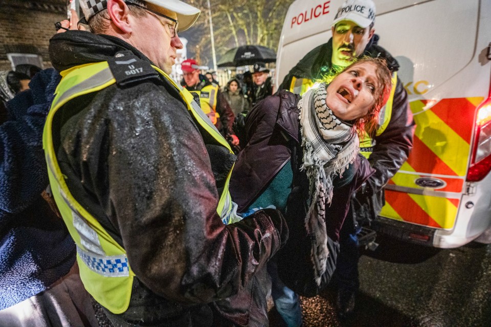 A Pro-Palestinian demonstrator in a keffiyeh scarf screaming as a police officer arrests her.