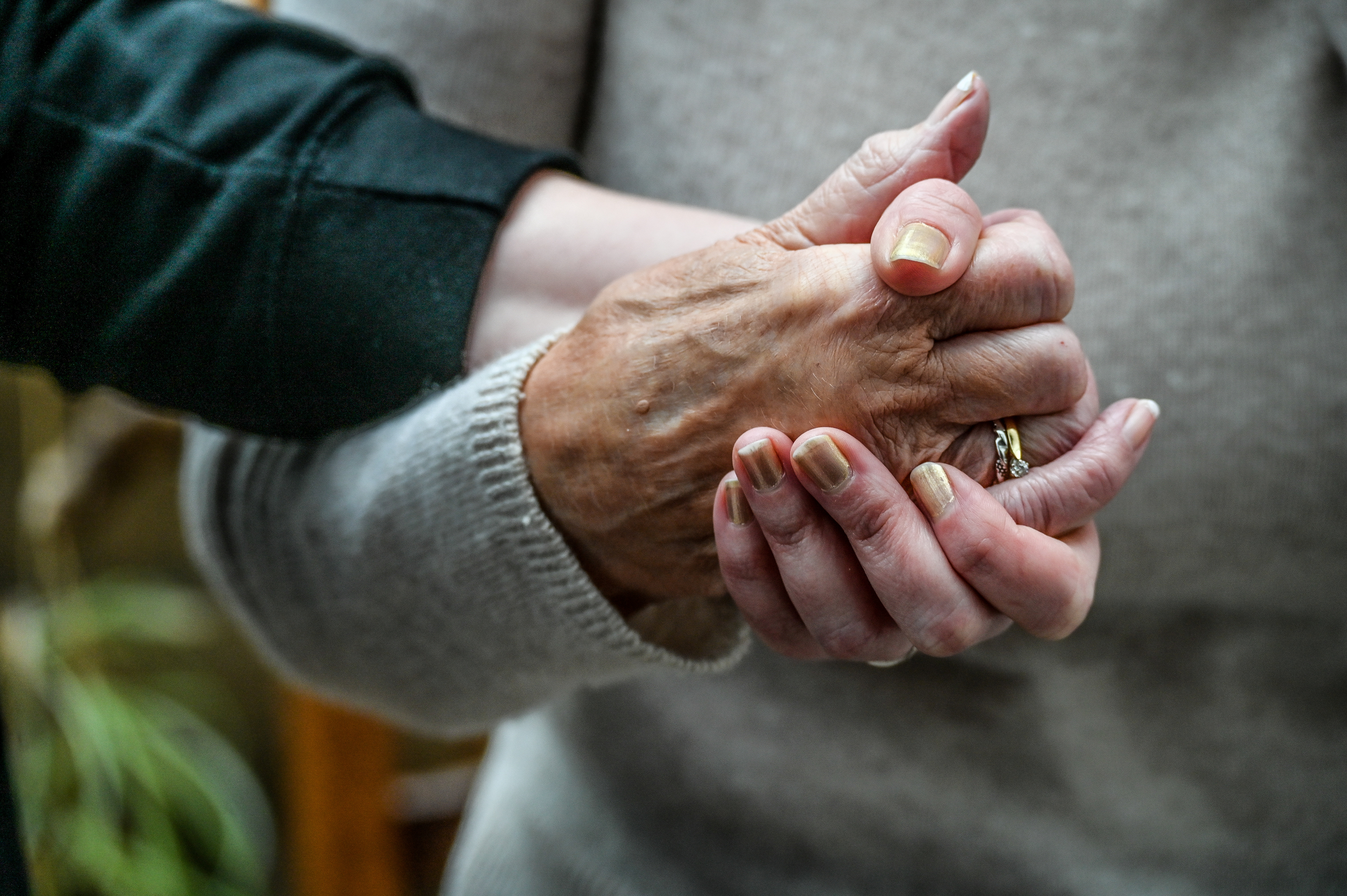 Two hands clasped, an older, wrinkled hand on top of a younger, smoother one.