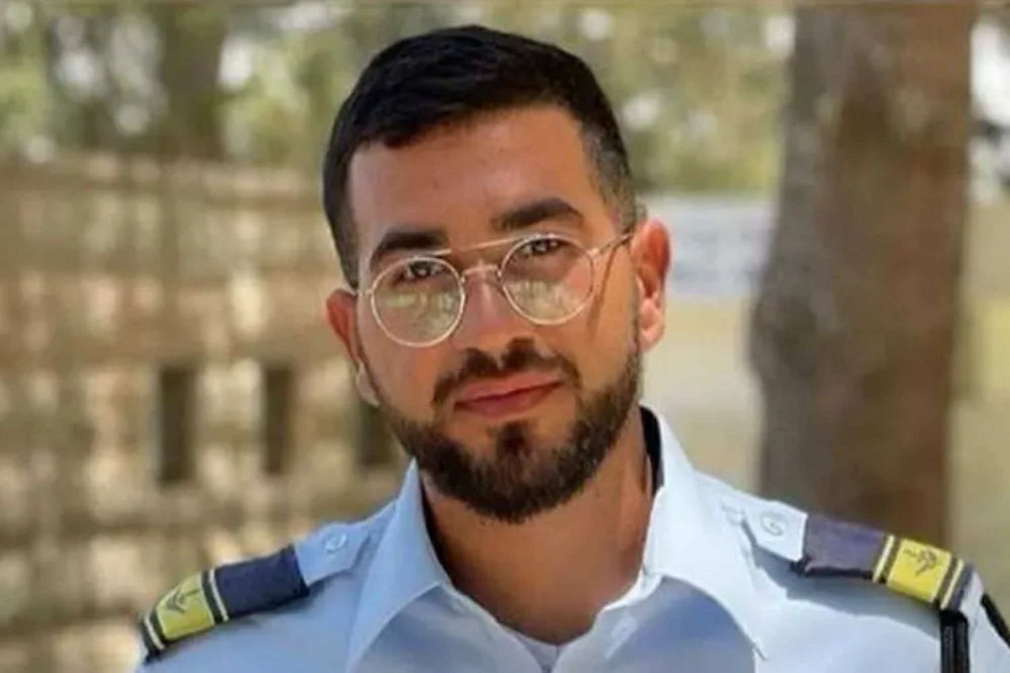 An image collage containing 1 images, Image 1 shows Ran Gvili, a hostage, wearing a light blue uniform shirt with epaulets, a beard, and glasses