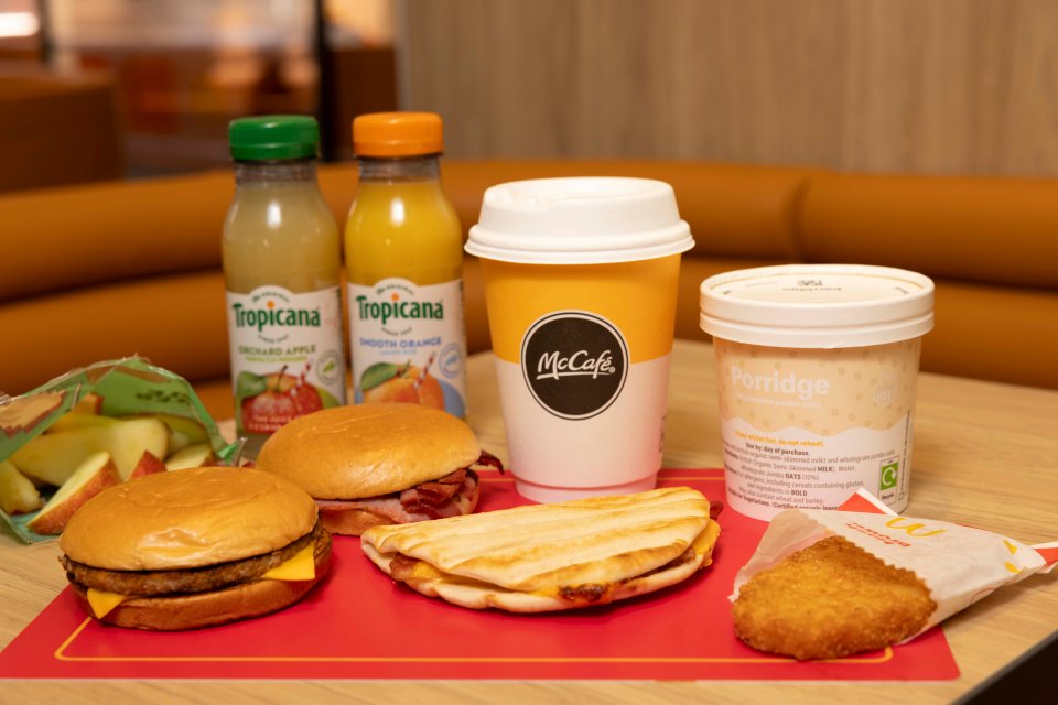 McDonald's breakfast: two sandwiches, hash brown, porridge, coffee, apple slices, and juice boxes.