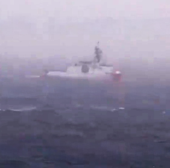 A white and red warship on dark blue, choppy water.