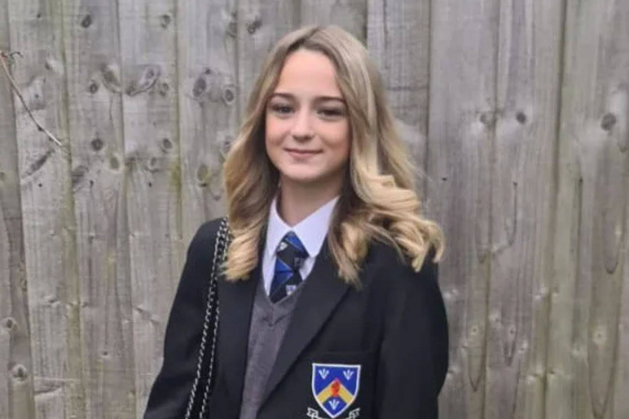An image collage containing 1 images, Image 1 shows A young girl wearing a school uniform stands outside in front of a wooden fence