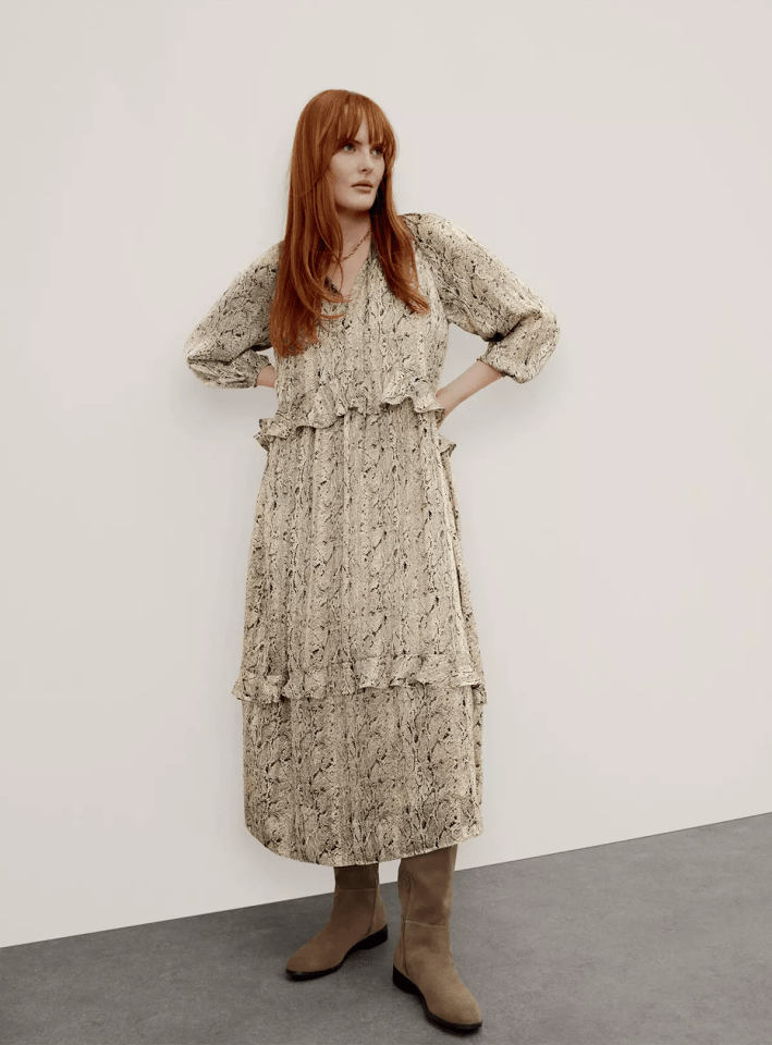 A woman with long red hair wearing a snakeskin print midi dress with ruffles and tan boots.