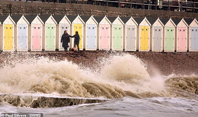 Dog walkers pass strong waves hitting the coastline of Lyme Regis in Dorset this afternoon