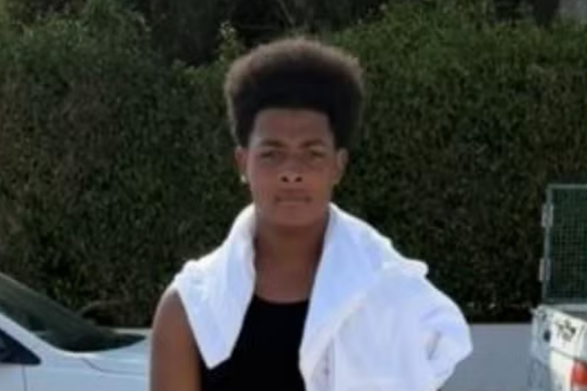 An image collage containing 1 images, Image 1 shows Maliki, a young man, stands in front of green bushes and parked cars