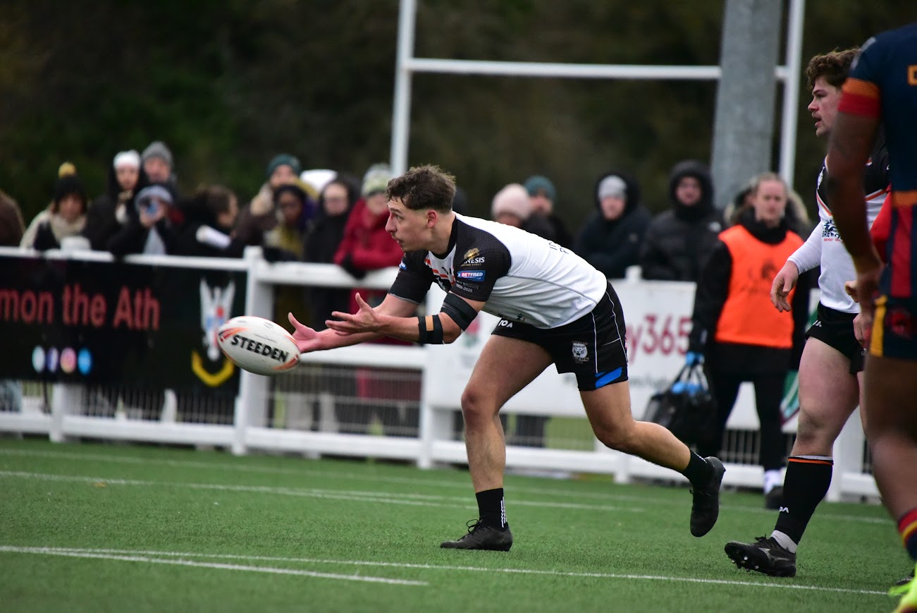 A rugby player in a white and black jersey prepares to catch a Steeden rugby ball.