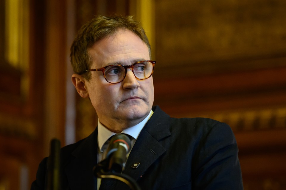 Tom Tugendhat, MP for Tonbridge, wearing glasses and a suit, looks away from the microphone in front of him.