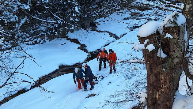 Four people in winter gear and helmets navigating a snow-covered landscape next to a frozen stream.