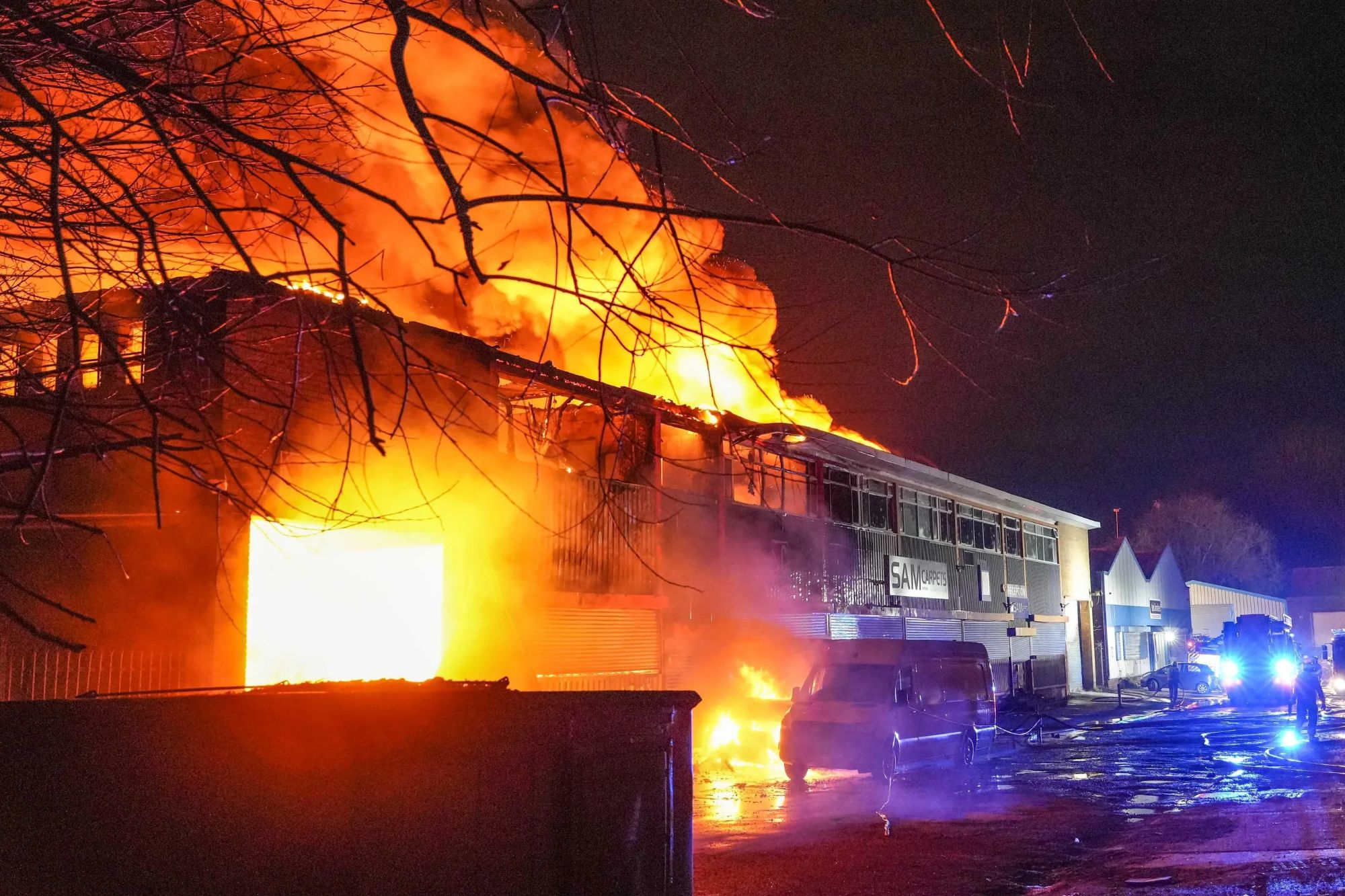 An image collage containing 1 images, Image 1 shows Fire engulfing the "Sam Carpets" warehouse in Birmingham, with visible flames, smoke, and fire crews on site