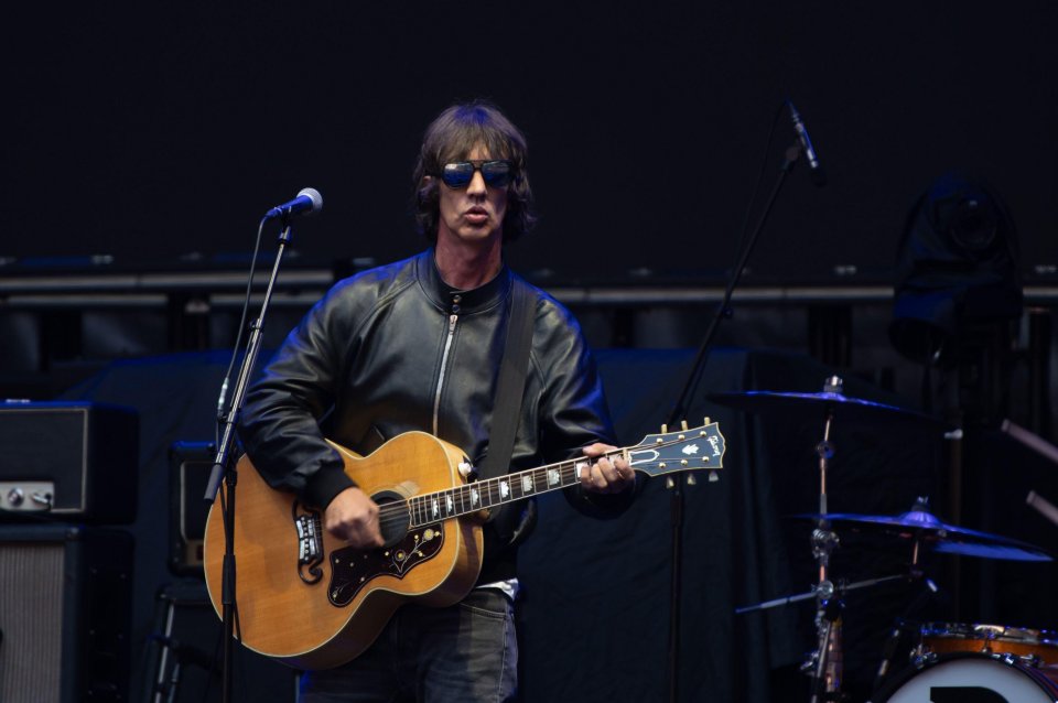 Richard Ashcroft performs on stage with an acoustic guitar and sunglasses.