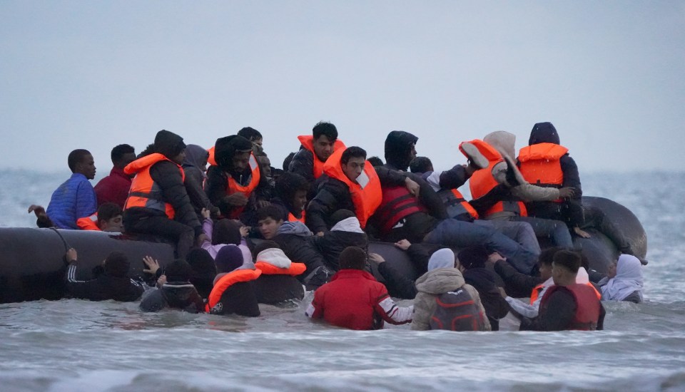 Migrants wearing life vests attempt to board a smuggler's boat from the water.