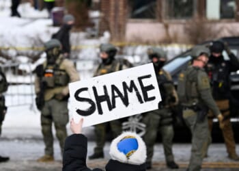 An onlooker holds a sign that reads "Shame" as members of law enforcement work the scene following a suspected shooting by an ICE agent during federal law enforcement operations on Jan. 7, 2026, in Minneapolis, Minnesota.