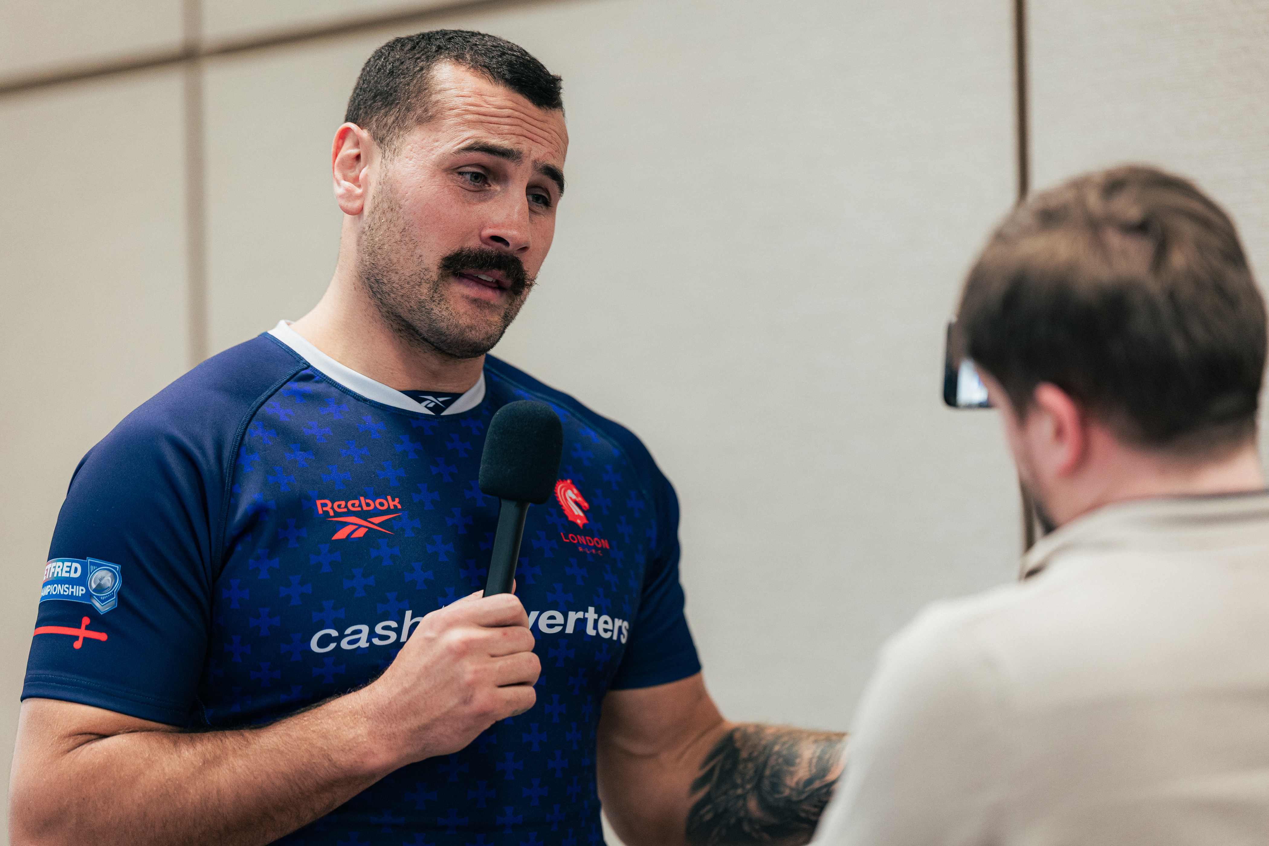A rugby player in a blue and red jersey speaking into a microphone.