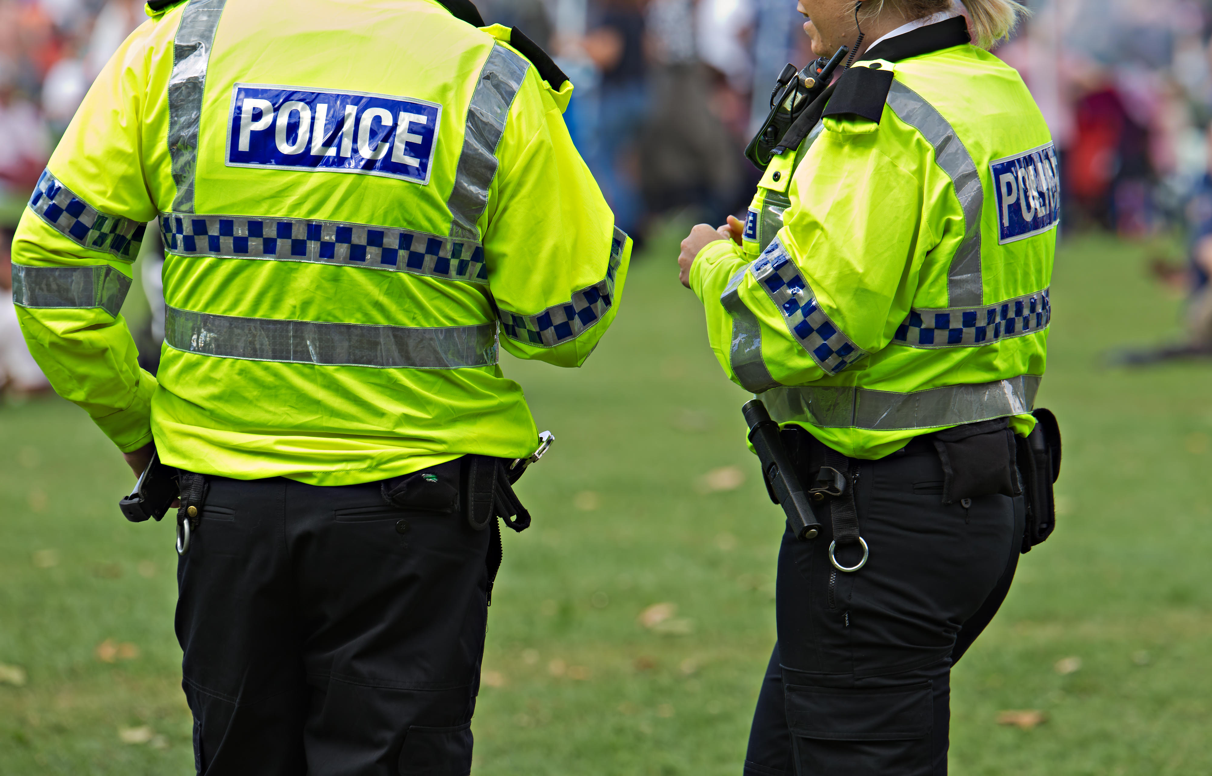 Two British police officers in neon yellow jackets with "POLICE" written on the back.