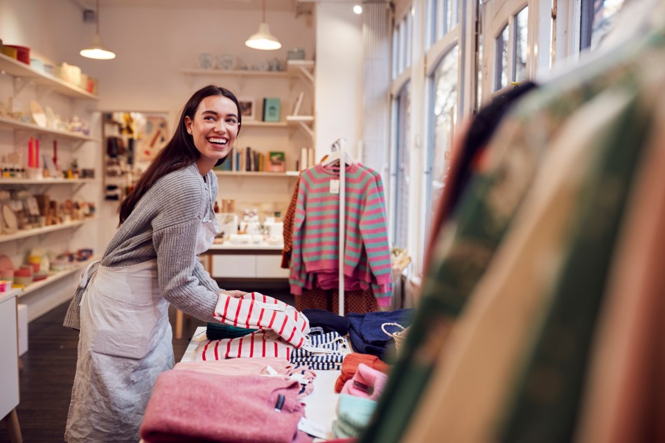 A smiling female small business owner arranging stock in a window display.