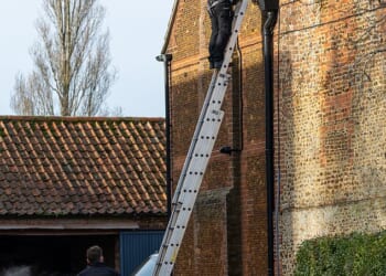 A Sky engineer up a ladder against the wall of Marsh Farm. The technicians were wearing uniforms with Sky VIP written on them