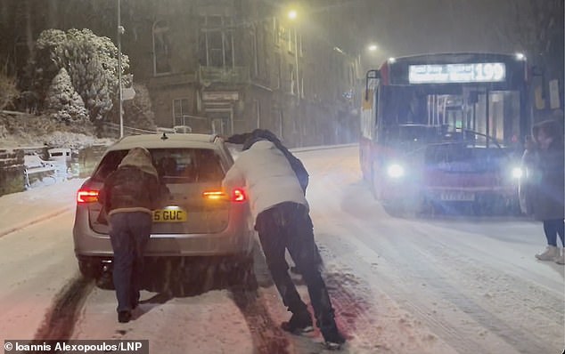 People attempt to push a car stuck in the snow in Buxton, Peak District, Derbyshire, on Thursday night