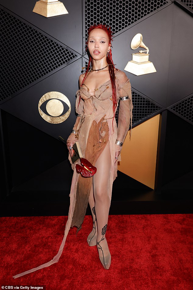 Missed the mark! FKA Twigs donned a very interesting, neutral-colored mesh ensemble as she walked the red carpet on Sunday night. The dress, which looked like it was made from different pieces of cloth, featured a low-cut neckline and slit in the thigh. She matched it with a pair of neutral, fishnet tights with rose detailing at the feet, placing the tights over her heels. FKA Twigs completed the look by holding a red flower in one hand
