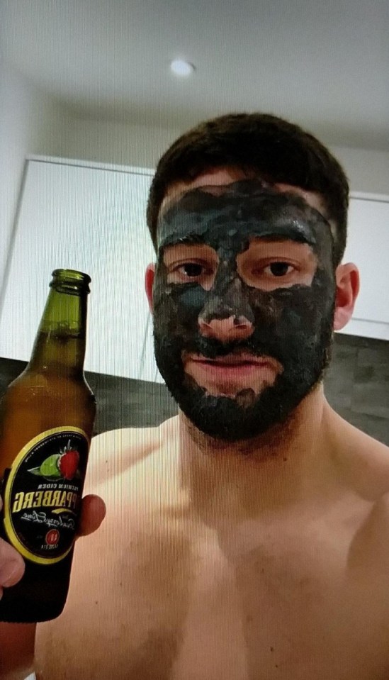 Man with a mud mask on his face holding a bottle of cider.