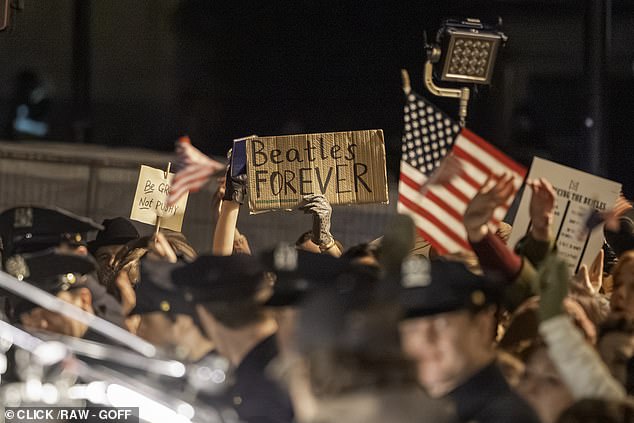 A similar banner is brandished by an extra while reenacting the chaotic street scene