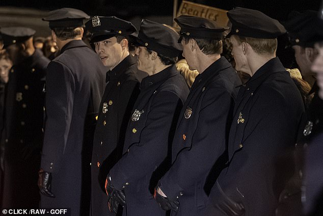 Actors in police uniform create a protective gauntlet for the band as they recreate their 1964 arrival in New York City