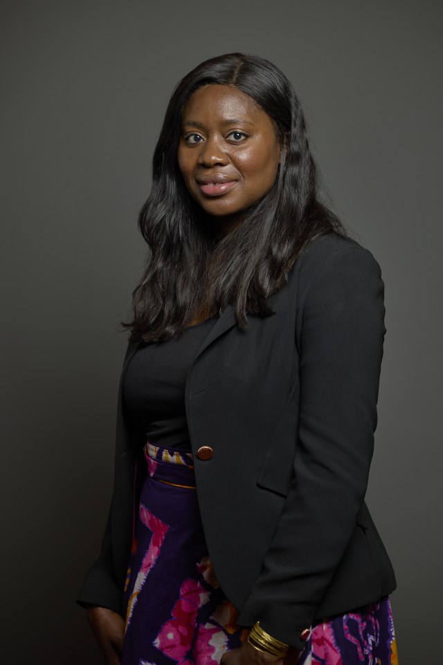 Portrait of a woman with long dark hair, wearing a black top and blazer, and a colorful purple, pink, and yellow patterned skirt.