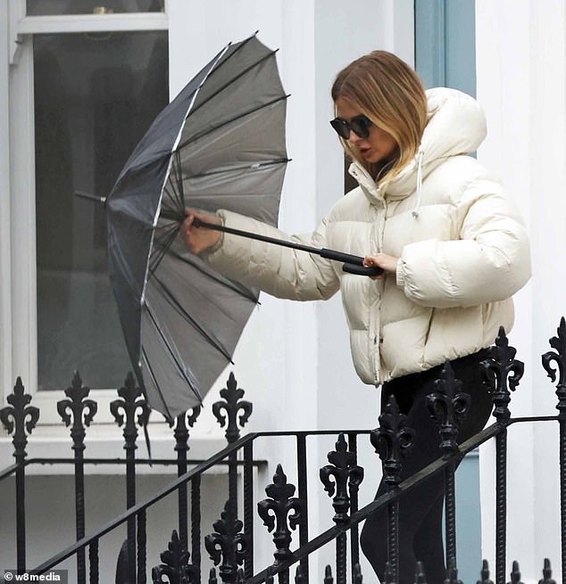 Millie sheltered from the rain with an umbrella as she headed out in a white padded jacket, black leggings and Nike trainers