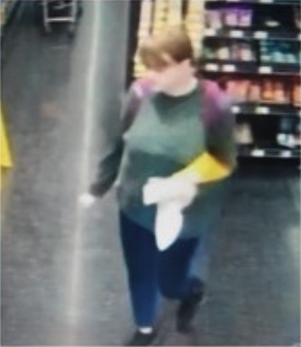A person walks through an aisle in a store, holding a yellow glove and white cloth.