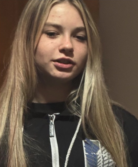 A young woman with long blonde hair and a black zippered top.