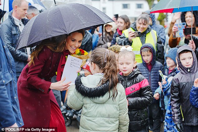 Despite the downpour, members of the public gathered in large crowds as Kate is seen accepting a handwritten letter from a fan