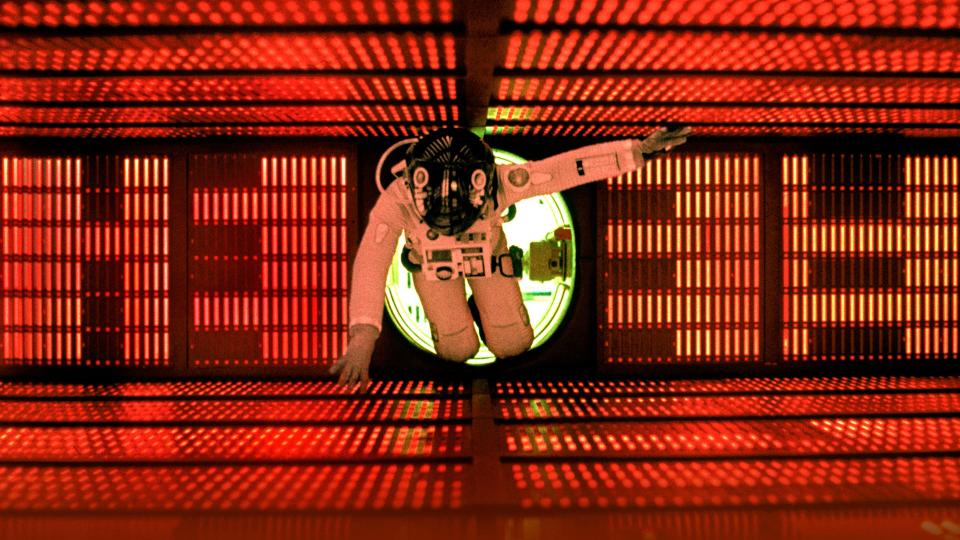 An astronaut in a white suit and black helmet floats through a red-lit tunnel.