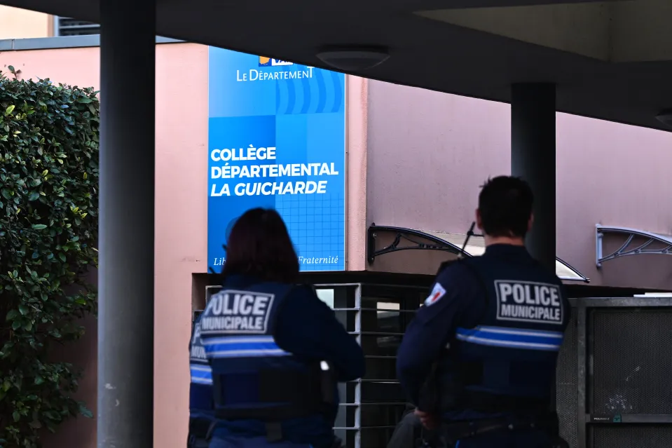 Two municipal police officers stand guard in front of the Collège Départemental La Guicharde.
