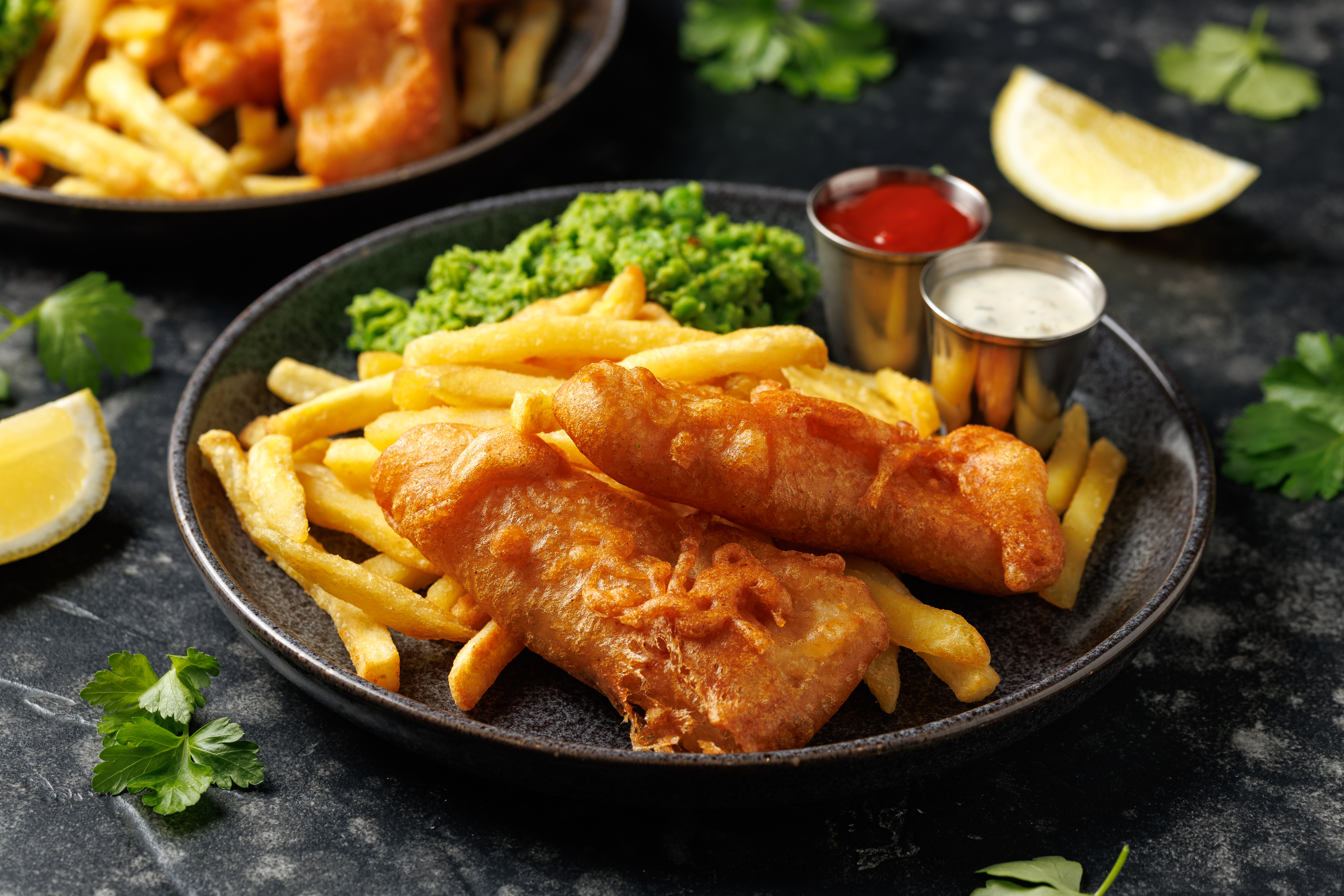 Fish and chips with mashed peas, tartar sauce, ketchup, and lemon.