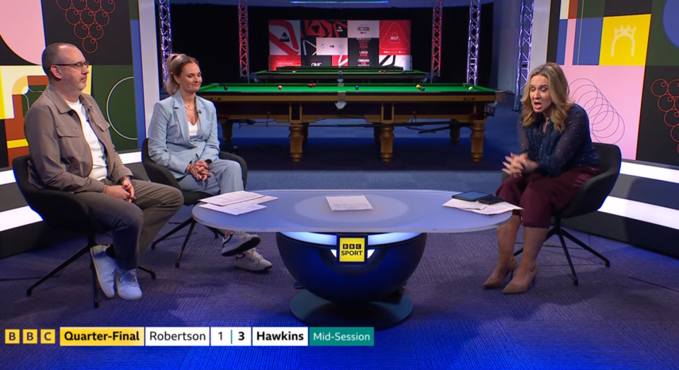 Three commentators discuss a snooker match in a studio, with the snooker table visible behind them.