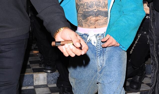Justin Bieber was seen keeping a low profile as he left his Grammy after-party at The Bird Streets Club in West Hollywood, covering his face with his arm while wearing an open teal hoodie over a bare chest, loose blue jeans, and casual slip-on shoes
