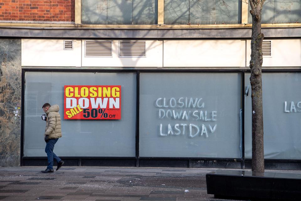 A man walks past a former Debenhams store advertising a "CLOSING DOWN SALE" with "50% off for Refurbishment" and "LAST DAY."