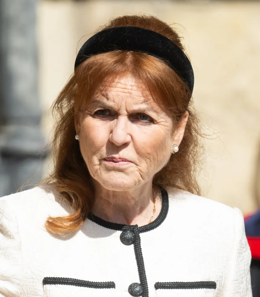 Older woman with red hair and a black headband, wearing a white jacket with black trim.