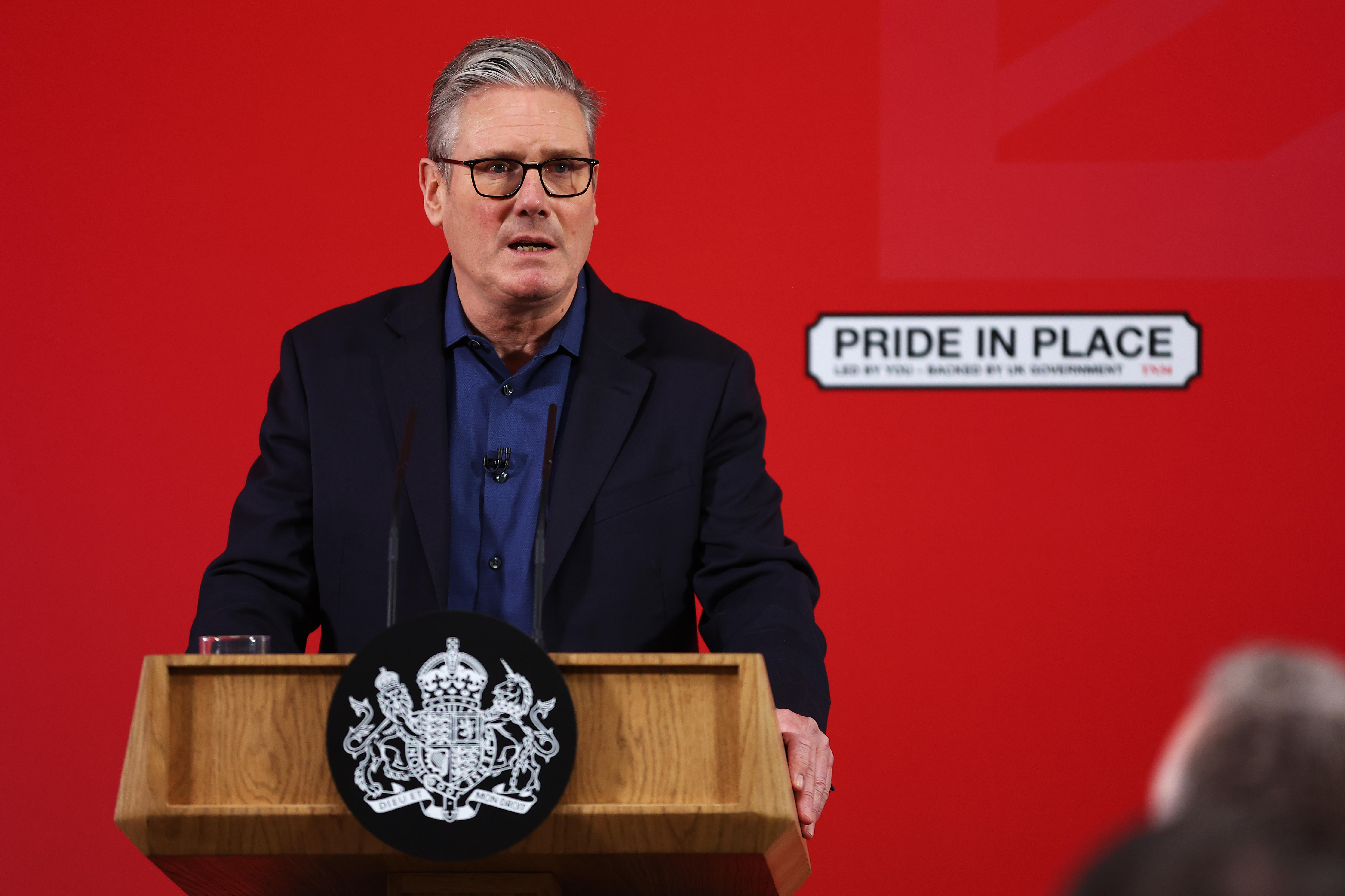 Keir Starmer speaking at a podium against a red background with a "Pride in Place" sign.