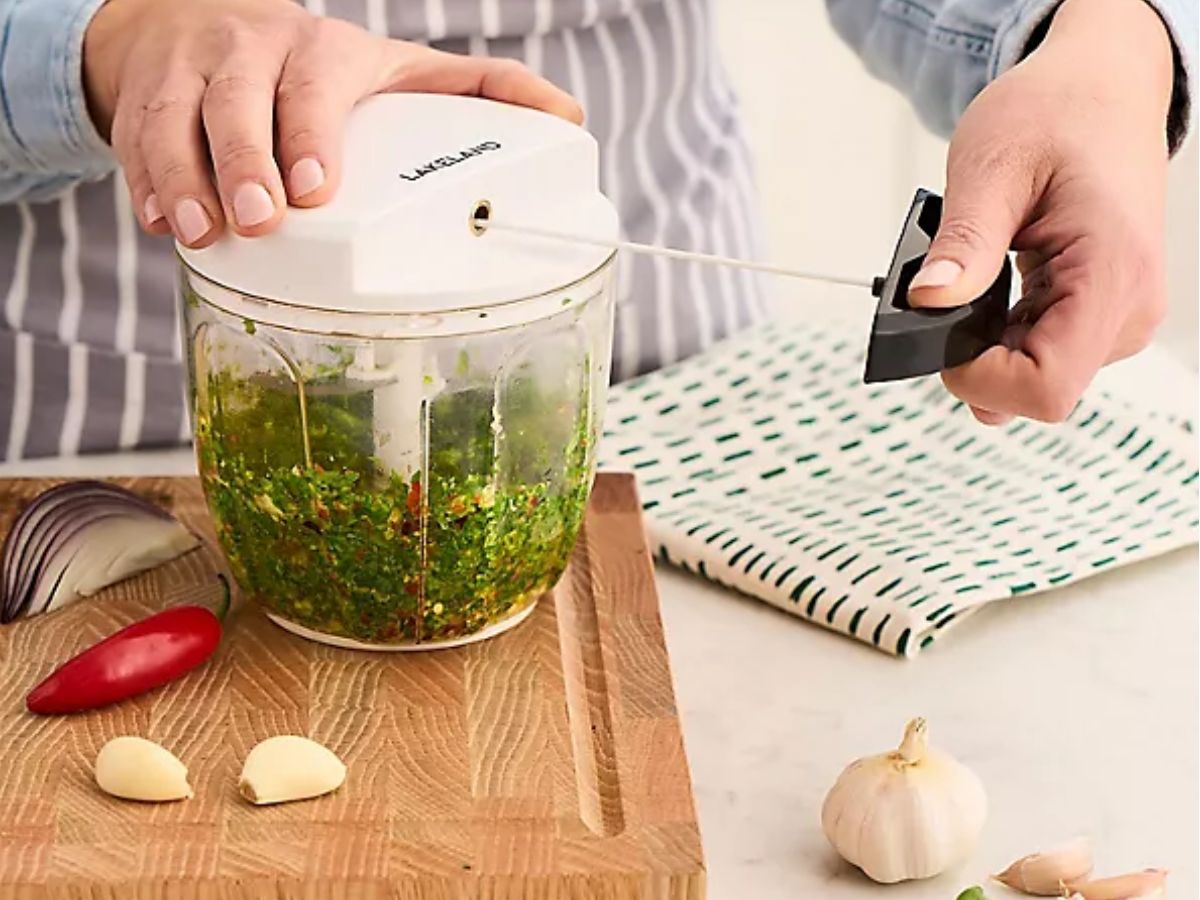 A person operating a manual food chopper filled with green pesto.