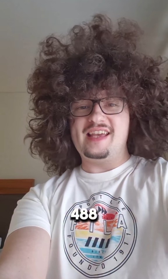 A man with large, curly brown hair and glasses smiling at the camera.