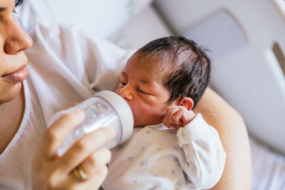 Mother feeds newborn baby with bottle in hospital room.