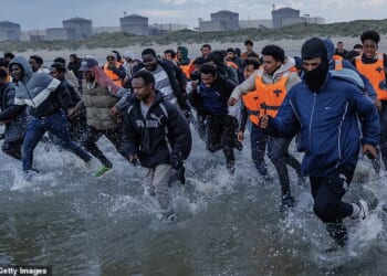 Migrants sprint across the beach at Gravelines, northern France, to board a smugglers' dinghy to Britain last summer