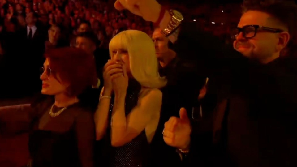 Kelly Osbourne with hands over mouth in a crowd.