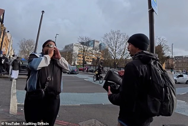 The man wearing sunglasses and a black, blue, and white tracksuit top repeatedly bellows a derogatory remark